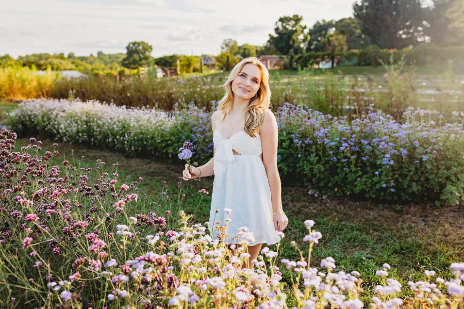 Madelyn Wright standing in a garden of purple and white wildflowers, holding a single lavender bloom